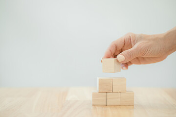 Hand putting wood cube block on top pyramid on table with copyspace, With the concept of a thriving business going for success..