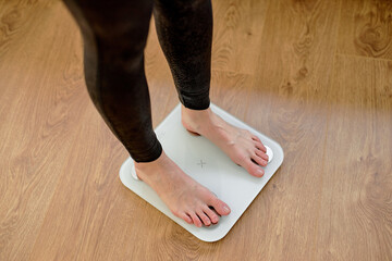 cropped unrecognizable woman in leggins stepping on floor scales indoors, sport and healthy lifestyle. Overweight problem