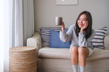 Obraz premium Portrait image of a young woman raising hand and say hi to friends outside while drinking coffee at home