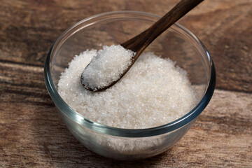 sugar in a wooden tea spoon and sugar in a glass bowl