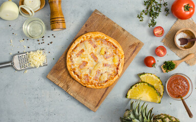 Top view shot of delicious tasty juicy of Hawaiian traditional Italian crust thin crispy ham and pineapple pizza placed on wooden cutting board with ingredients sliced tomatoes, ketchup and salt