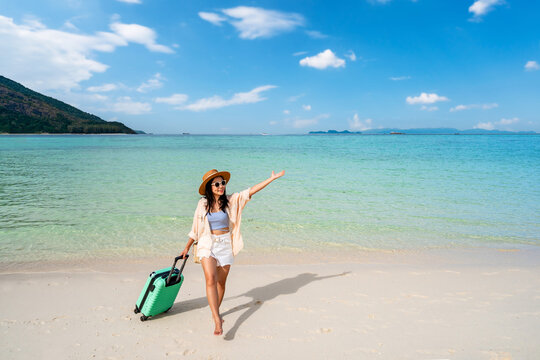 Young woman traveler with luggage relaxing and enjoying at beautiful tropical sand beach, Summer vacation and Travel concept