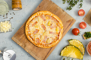 Top view shot of delicious tasty juicy of Hawaiian traditional Italian crust thin crispy ham and pineapple pizza placed on wooden cutting board with ingredients sliced tomatoes, ketchup and salt