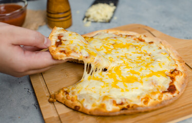 Closeup shot of unrecognizable unknown human hand picking up piece of delicious tasty double cheese traditional Italian crust thin crispy pizza up stretching cheese ready for dinner serve.