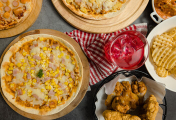 Top view shot of various kinds of delicious tasty juicy cheesy pizza placed on wooden board on party table around with other fast food  for eating dinner together.