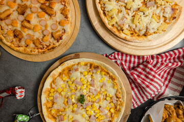 Top view shot of various kinds of delicious tasty juicy cheesy pizza placed on wooden board on party table around with other fast food  for eating dinner together.