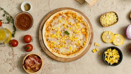 Top view shot of delicious tasty juicy cheesy corn and ham Italian pizza placed on wooden board on party table around with other ingredients, sauce, olive oil, bacon, tomatoes, cheese and vegetables