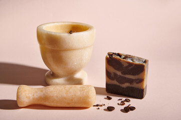 Still life. A marble mortar with pestle and cold-pressed homemade natural soap with organic ingredients and coffee beans for body skin care on a pink background. Body scrub. Spa and hygiene concept