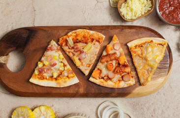 Top view shot various kinds of delicious tasty juicy thin crispy cheesy sliced Italian pizza placed on wooden cutting board on party table around with other ingredients, sauce, corn, cheese, tomatoes