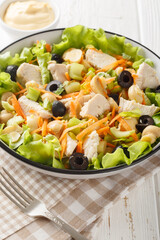 Chicken salad with mushrooms, carrots, celery, olives, cheese and lettuce close-up in a bowl on a wooden table. Vertical