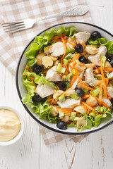 Chicken salad with mushrooms, carrots, celery, olives, cheese and lettuce close-up in a bowl on a wooden table. Vertical top view from above
