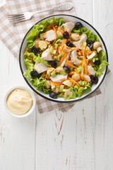 Italian Piedmontese salad with chicken, mushrooms, carrots, celery, olives, cheese and lettuce close-up in a bowl on a wooden table. Vertical top view from above