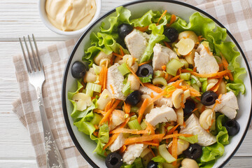 Healthy diet salad with chicken, mushrooms, carrots, celery, olives, cheese and lettuce close-up in a bowl on a wooden table. Horizontal top view from above