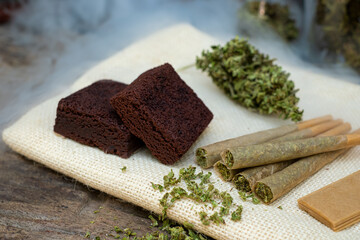 Pre-Roll cannabis joints and cake brownies with Marijuana buds laying on the sackcloth