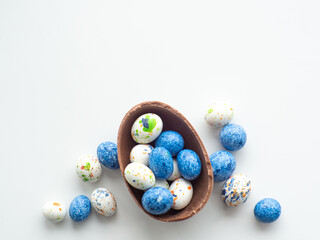 Sweet Easter concept. Blue, white and chocolate easter eggs with sweet dragee on white background with copy space. Design for a greeting card for the Easter holiday. Flat lay. Preparation for holiday.