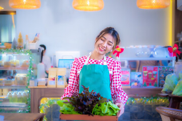 Beautiful asian waitress wearing an apron holding a wooden tray full of organic vegetables with a smile while her eyes close, Smart farm, Harvesting.