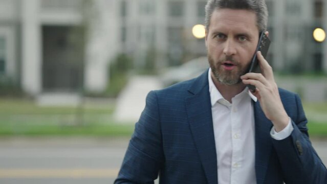 Business man walking on street and speaking phone. Mature business man talking on phone outdoor. Businessman in a formal suit using phone.
