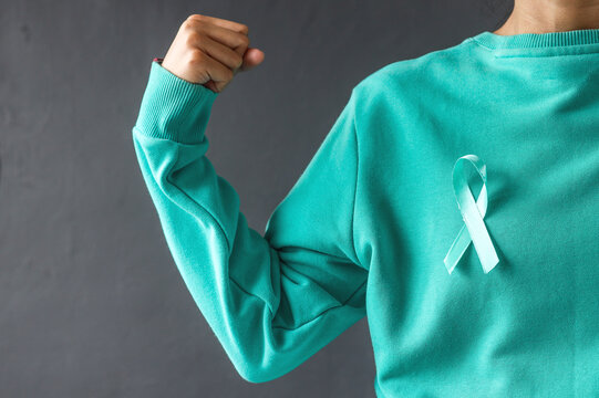 Woman hands wearing teal t-shirt and teal awareness ribbon gesturing strong hand . Support cancer survivor. Ovarian Cancer month, cervical cancer day. 