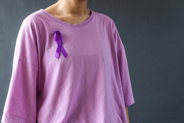 Woman wearing purple t-shirt and purple ribbon to support cancer survivor on grey background....