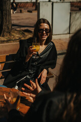 A shot of young beautiful girl holding a glass of cocktail and smiling while sitting at the coffee bar with her friends on a beautiful sunny day