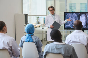 Female doctor pointing at monitor with x-ray image of lungs and discussing disease with her...