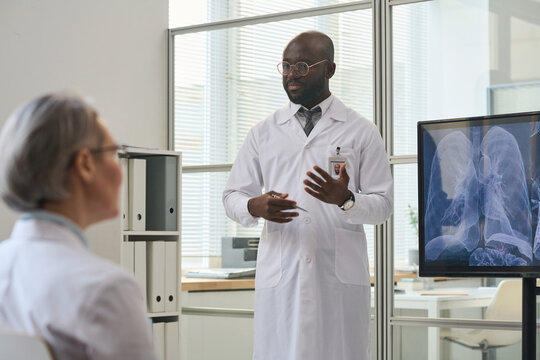 African American doctor in white coat presenting x-ray image of lungs to his colleagues during conference