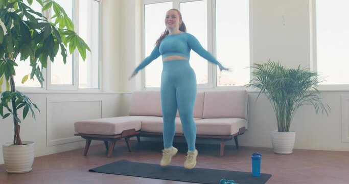 happy smiling woman enjoying doing jumping jacks at home. Sportswoman doing jumping jacks exercise at home. fat woman jumping with raised arms, girl doing sport, losing weight