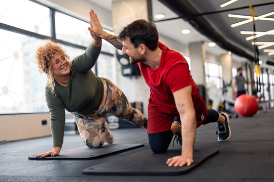 Active couple giving each other high-five for support in push ups, plank and balance training during fitness workout exercise in gym. Fitness motivation and high five while exercising together in gym.