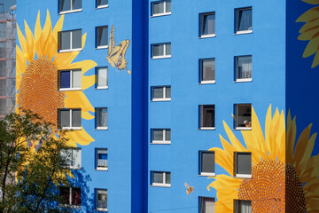 artistically painted house, skyscraper reaching for the sky, with sunflower blossoms on blue house wall, windows, mural painting, copy space