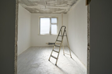 Interior of a new apartment without finishing in gray tones with folding metal ladder-step ladder.