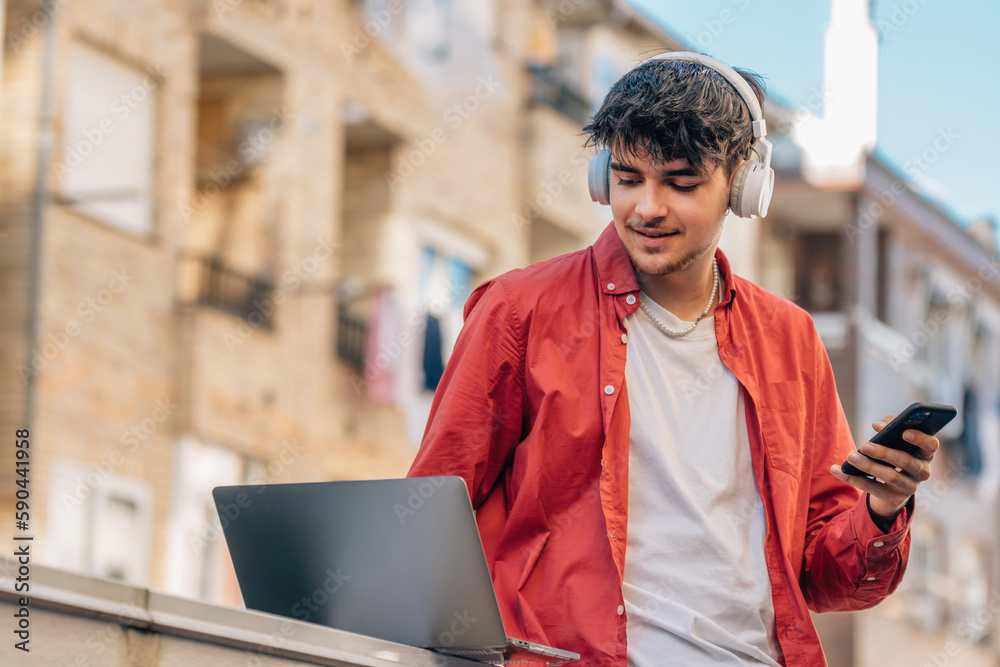 Poster young man with smartphone or mobile phone, laptop and headphones outdoors in the city