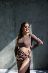 Fototapeta na wymiar A happy young pregnant woman in a brown delicate suit is posing and stroking her belly. Pregnant pregnant woman. Happy pregnancy