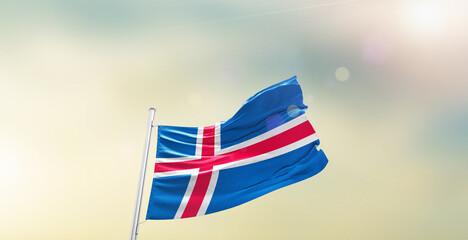Waving Flag of Iceland on blur sky. The symbol of the state on wavy cotton fabric.