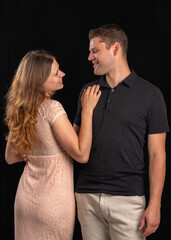 A girl with long hair stands backwards with a beautiful figure and looks at the guy. Black background. Contrast light dress and black T-shirt. Love, relationships