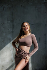 Fototapeta premium A happy young pregnant woman in a brown delicate suit is posing and stroking her belly. Pregnant pregnant woman. Happy pregnancy