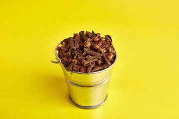 A small metal bucket filled with clove spices on a yellow background.
