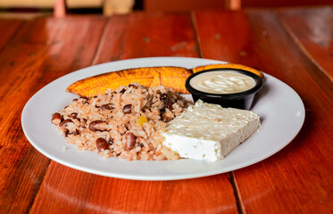 Traditional Gallo Pinto meal with maduro and cheese served. Gallopinto plate with cheese and maduro on wooden table. Nicaraguan food concept
