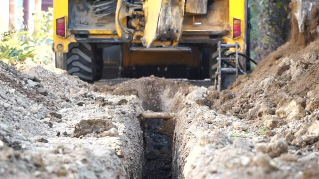 Excavator digs a trench to lay pipes. Close up of an excavator digging a deep trench. An excavator digs a trench in the countryside to lay a water pipe. Slow motion