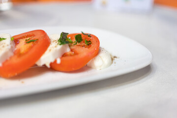 Italian Caprese Salad with Mozzarella cheese, tomatoes, basil, olive oil on white plate at Italian diner, restaurant. Fresh Caprese is traditional Italian food from Italy. Traditional food concept.
