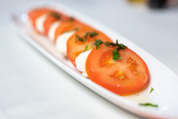 Italian Caprese Salad with Mozzarella cheese, tomatoes, basil, olive oil on white plate at Italian diner, restaurant. Fresh Caprese is traditional Italian food from Italy. Traditional food concept.