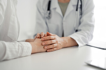 Doctor and patient sitting at the desk in clinic office. The focus is on female physician's hands reassuring woman, close up. Perfect medical service, empathy, and medicine concept