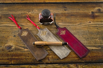 Leather bookmarks lay down to wooden table with a fountain pen and ink
