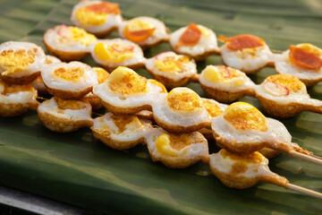 Fried Quail eggs in bamboo skewers on pothole pan. Drop each egg in a small ramekin gently slide it into the hot oil. Serve warm with salt and ground pepper. Thai appetizer at street food market.
