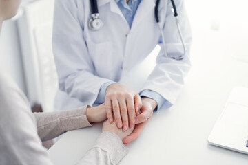 Doctor and patient sitting at the table in clinic office. The focus is on female physician's hands...