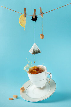 Tea bag, lemon and sugar hanging on the rope over splashing tea on blue background. Creative still life concept.