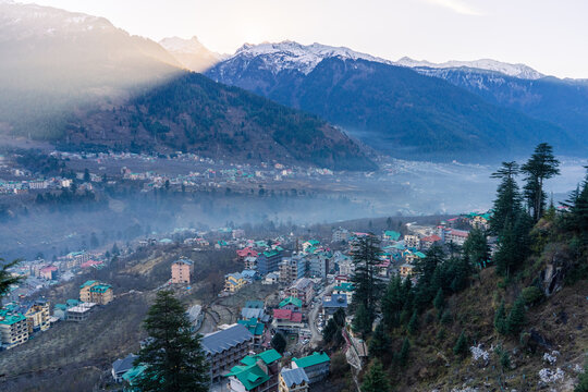 monsoon clouds moving over snow covered himalaya mountains with the blue orange sunset sunrise light with town of kullu manali valley at the base of mountains