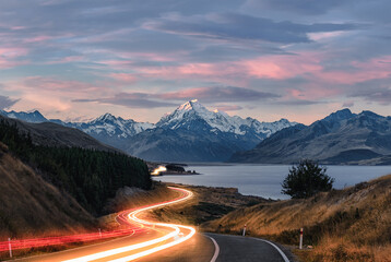 Road to Mt Cook in New Zealand during sunset. Traffic is causing light trails leading to the mountain.  - obrazy, fototapety, plakaty