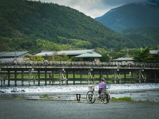 Young boy with a bicycle sitting by the river and looking at the green mountains