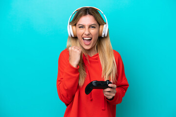 Young Uruguayan woman playing with a video game controller isolated on blue celebrating a victory in winner position © luismolinero