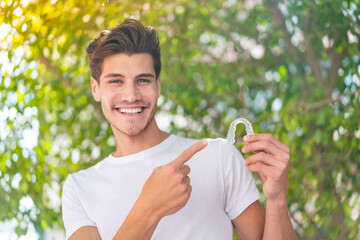 Young caucasian man holding invisible braces at outdoors and pointing it